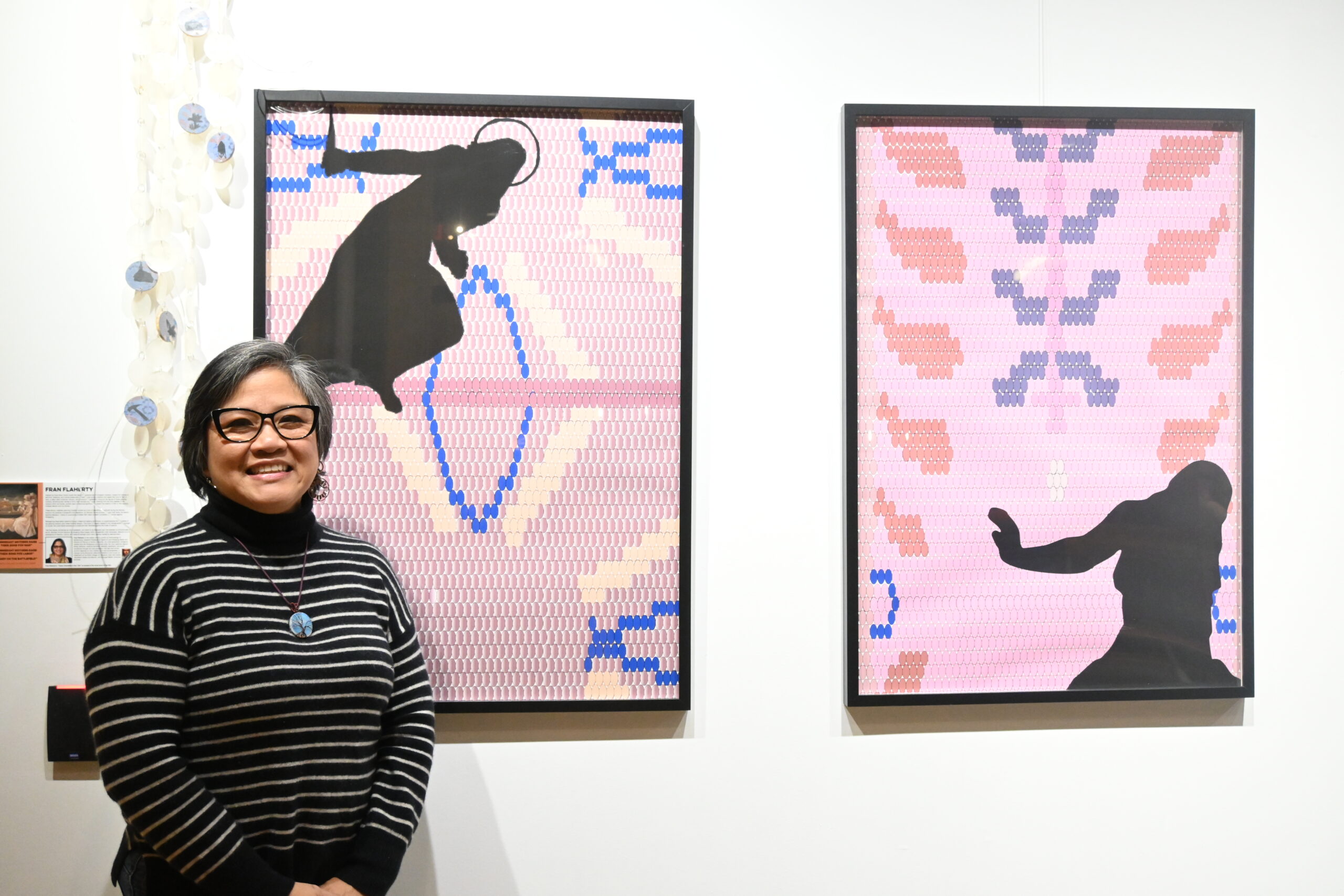 Artist Fran Flaherty stands along side two of her artworks hanging on a white wall.